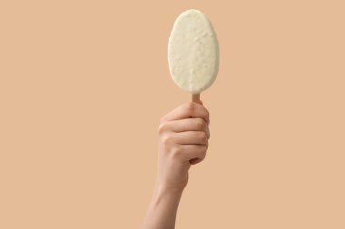 Elinde nefis çikolata kaplı dondurma tutan kadın bej arka planda.