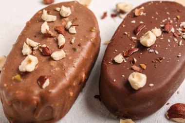Lezzetli çikolata kaplı dondurma, beyaz masada ezilmiş fındıklar, yakın plan.
