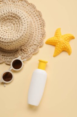 Güneş gözlüklü bebek için güneş kremi, bej arka planda şapka ve oyuncak