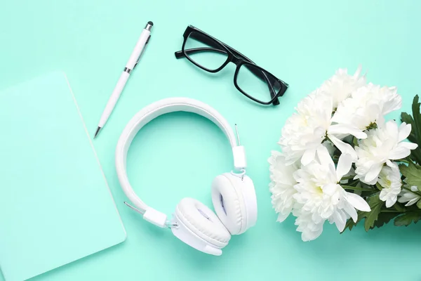 Modern headphones, eyeglasses, notebook, pen and chrysanthemum flowers on color background