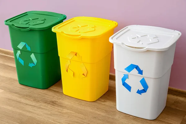 Garbage bins with recycling symbol near pink wall