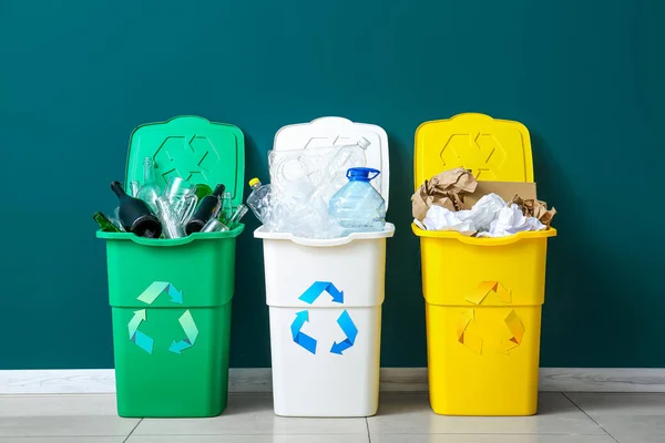 Trash bins with recycling symbol and different garbage near green wall