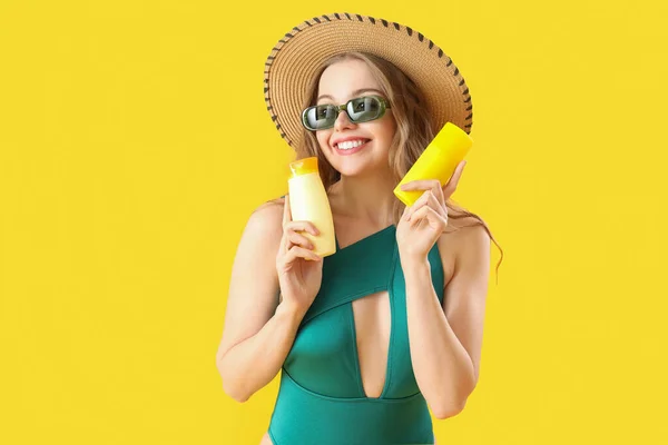 Beautiful young woman with sunscreen creams on yellow background