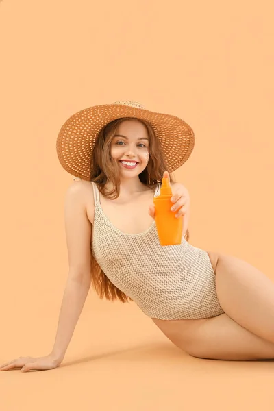 Beautiful young woman with sunscreen cream on beige background