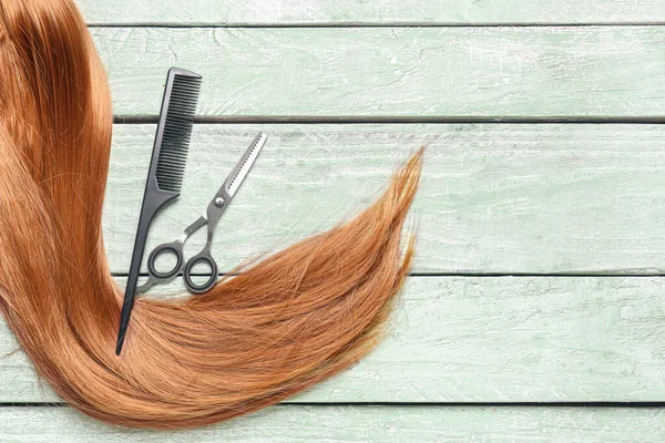 Ginger hair with brush and scissors on green wooden background