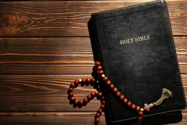 Holy Bible with prayer beads on wooden background