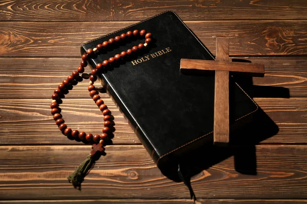 Holy Bible with cross and prayer beads on wooden background