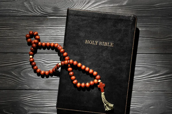 Holy Bible with prayer beads on black wooden background