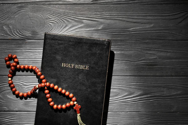 Holy Bible with prayer beads on black wooden background
