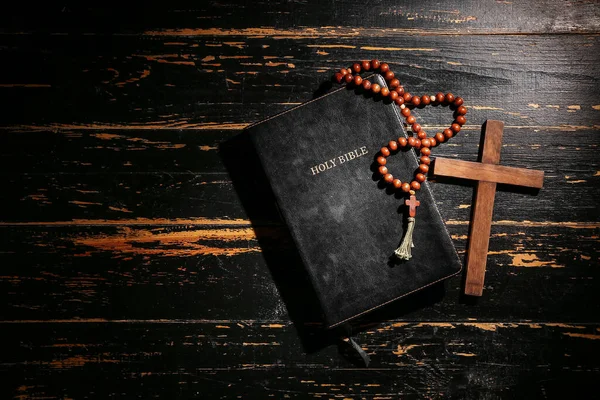 Holy Bible with prayer beads and cross on dark wooden background