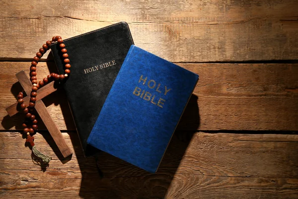 Holy Bibles with prayer beads and cross on wooden background