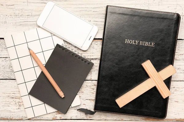 圣经上有手机 笔记本和白色木制背景的十字架 — 图库照片