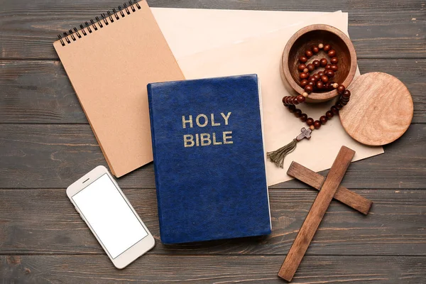 stock image Holy Bible with prayer beads, mobile phone, notebook and cross on wooden background