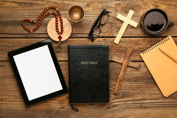 Holy Bible with prayer beads, tablet computer, eyeglasses and crosses on wooden background