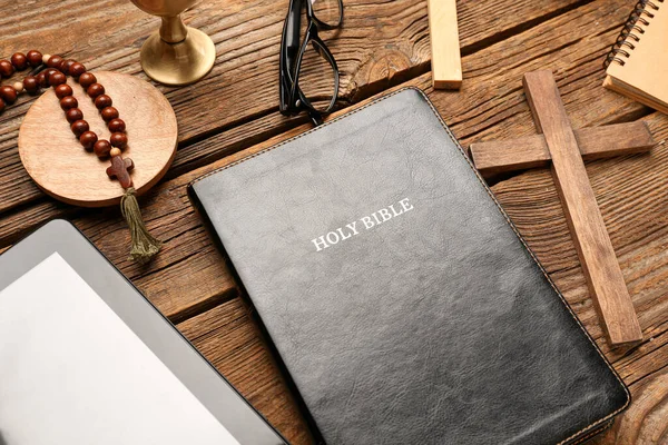 Holy Bible with prayer beads, tablet computer and cross on wooden background, closeup