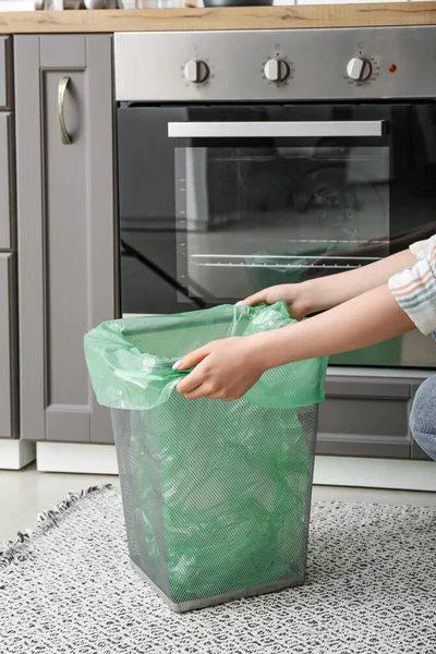 Woman placing garbage bag into trash bin in kitchen