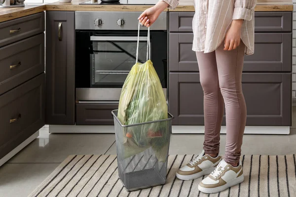 Woman taking full garbage bag from trash bin in kitchen