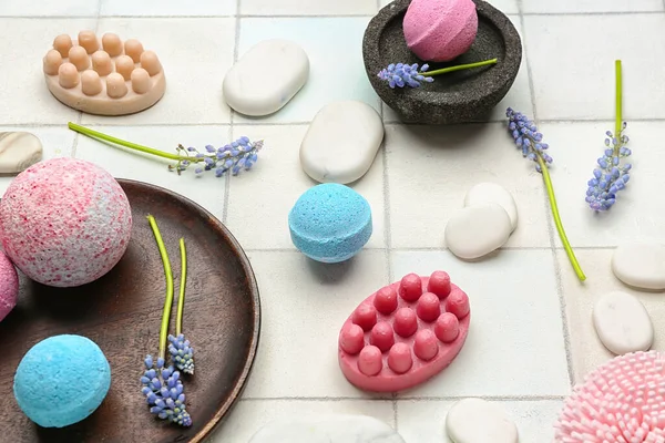 Bath bombs with flowers, soap bars and spa stones on white tile background