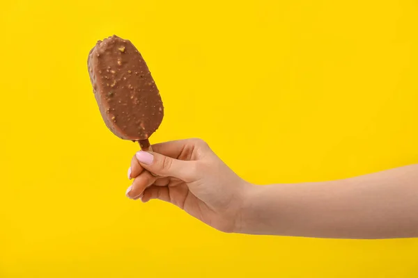 stock image Woman holding delicious chocolate covered ice cream on stick against yellow background