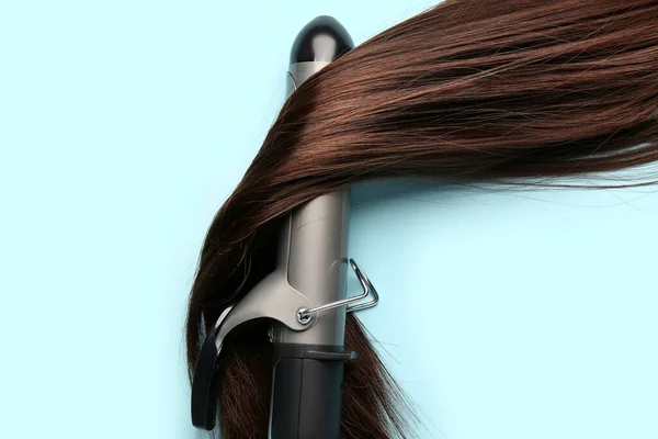 Brown hair with curling iron on blue background