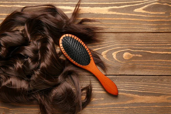 Curled brown hair with brush on wooden background