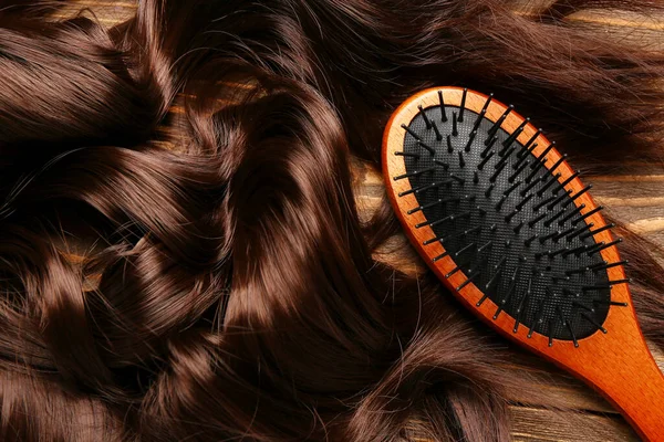 Curled brown hair with brush on wooden background, closeup