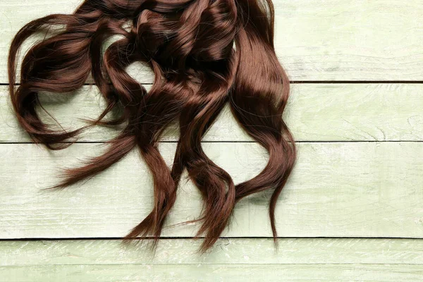 绿色木制背景的卷曲棕色头发 — 图库照片