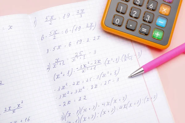 Copybook with maths formulas, pen and calculator on pink background