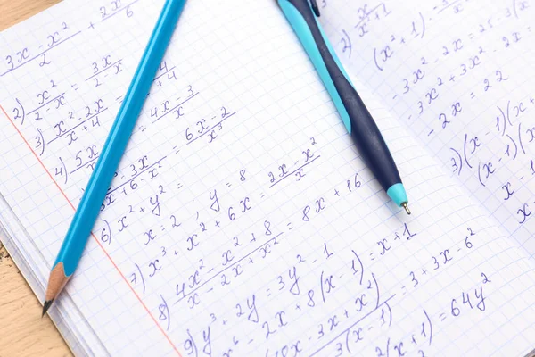 Copybook with maths formulas, pen and pencil, closeup