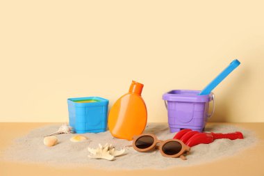 Plaj aksesuarlı bebek için bej duvarın yanındaki kumda güneş kremi.