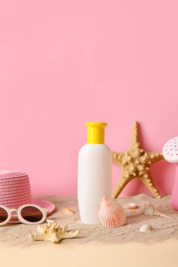 Pembe duvarın yanında kumsalda aksesuarları olan bebek için güneş kremi.