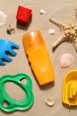Kumsalda aksesuarları ve deniz kabukları olan bebek için güneş kremi.