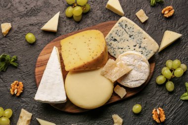Tahta tahta tahta tahta, farklı çeşitlerde lezzetli peynir, fındık ve üzümler koyu arka planda.