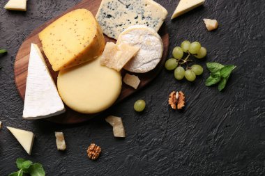 Tahta tahta tahta tahta, farklı çeşitlerde lezzetli peynir, fındık ve üzümler koyu arka planda.