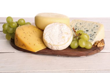 Masada beyaz arka planda farklı çeşit peynir ve üzümlü ahşap tahta.