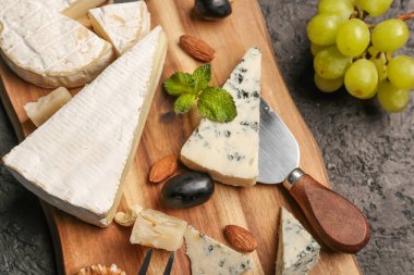 Koyu arka planda farklı çeşit lezzetli peynirli ahşap tahta, yakın plan.