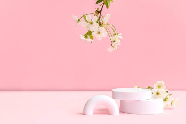 Pembe arka planda dekoratif podyumlar ve çiçek açan dallar