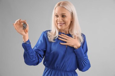 Evin anahtarlarını gri arka planda taşıyan olgun bir kadın.