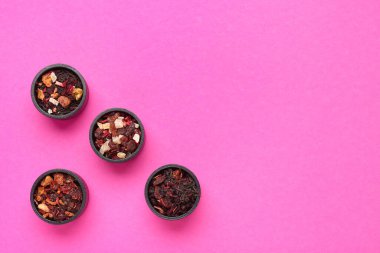 Pembe arka planda farklı kurutulmuş meyve çaylarıyla dolu kaseler.