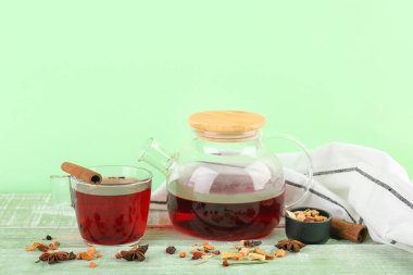 Çaydanlık ve bir bardak sıcak meyve çayı yeşil ahşap masada.