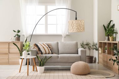 Oturma odasının içinde kanepe, lamba ve çiçek var.