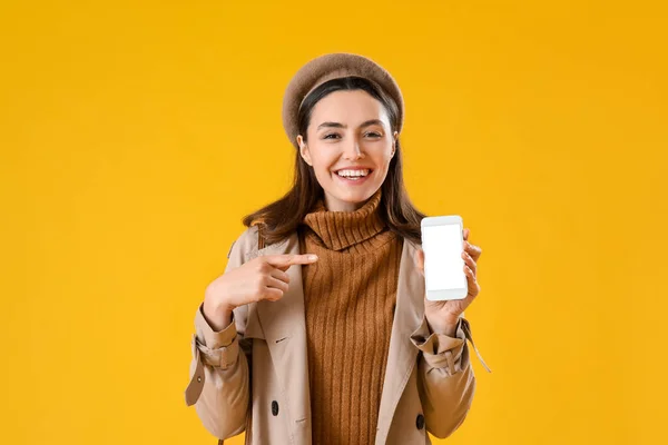 Молода Жінка Пальто Вказуючи Мобільний Телефон Жовтому Фоні — стокове фото