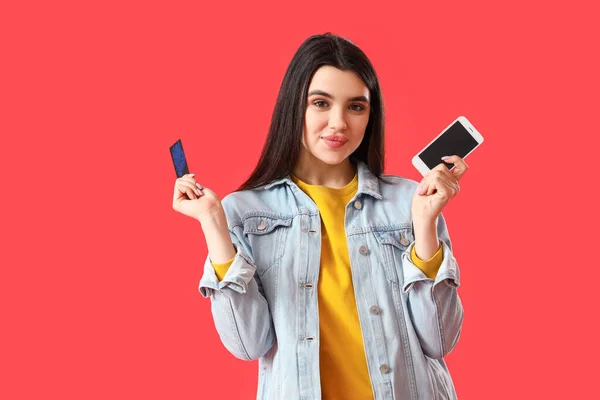 赤の背景に携帯電話とクレジットカードを持つかなり若い女性 — ストック写真