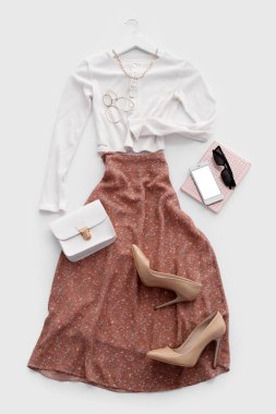 Aksesuarlı şık kıyafetler, topuklu ayakkabılar, cep telefonu ve beyaz arka planda not defteri.