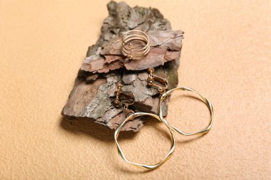 Altın küpeli ağaç kabuğu ve bej arka planda yüzük, yakın plan.