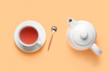 Turuncu arka planda seramik çaydanlık ve bir fincan çay.