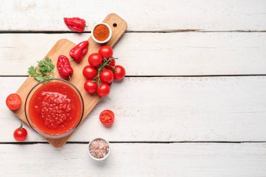 Lezzetli domates soslu kase ve beyaz ahşap arka planda taze sebzeler.