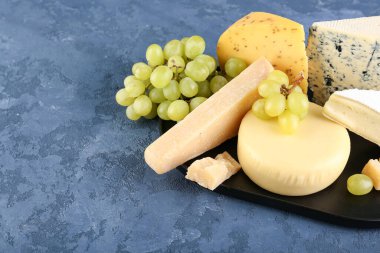 Mavi arka planda farklı peynir ve üzümlü tabak, yakın plan.