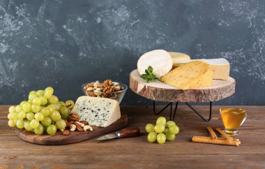 Masada değişik peynir, üzüm, bal ve fındık içeren tahta tahtalar.