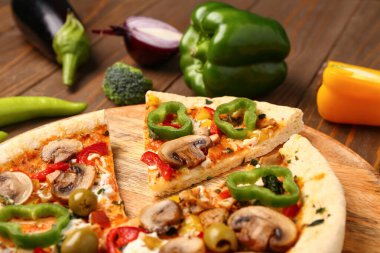 Tahtada sebze pizza ve ahşap arka planda malzemeler var.